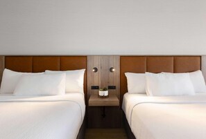 A hotel room with two beds, a wooden headboard, a small table with a plant, and a wall-mounted light fixture. - Valhalla Hotel and Conference Centre (Thunder Bay)