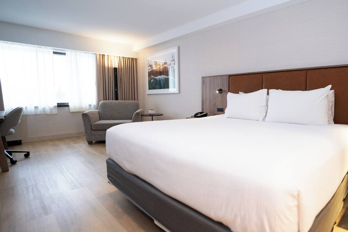 A hotel room with a large bed, a desk, a chair, a nightstand, and a painting on the wall.