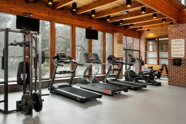 A gym with treadmills, a weight bench, and a TV screen.