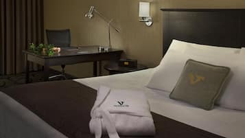 A hotel room with a bed, a desk, a chair, a lamp, and a nightstand.