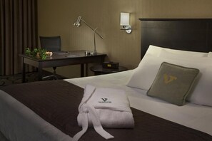 A hotel room with a bed, a desk, a chair, a lamp, and a nightstand.