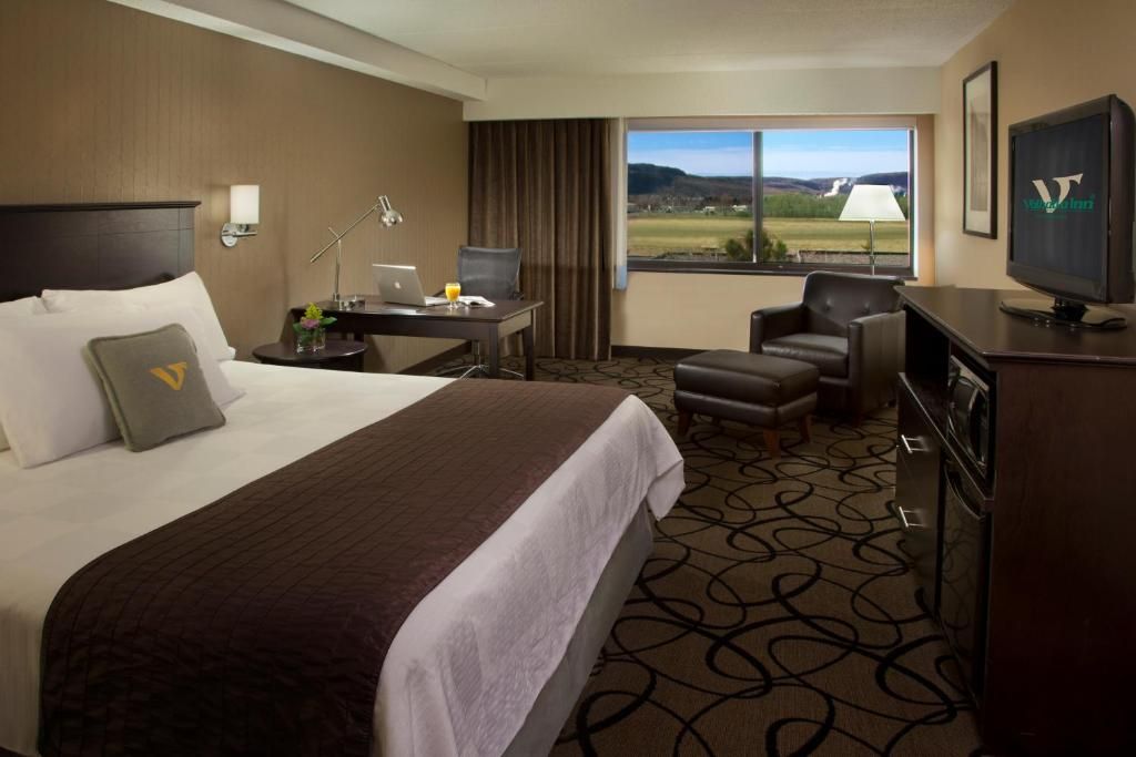 A hotel room with a bed, desk, chair, TV, and a view of the outdoors.