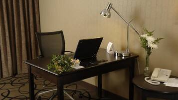 Habitación de hotel con escritorio, computadora portátil, teléfono, lámpara y un florero con flores.