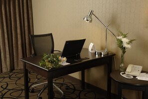 A hotel room with a desk, a laptop, a telephone, a lamp, and a vase with flowers.