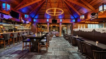 Un interior rústico con vigas de madera, una zona de bar y diferentes distribuciones de asientos.