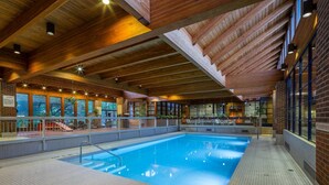 An indoor swimming pool with a tiled floor, wooden ceiling beams, and a view of the outdoors through large windows. - Valhalla Hotel and Conference Centre (Thunder Bay)