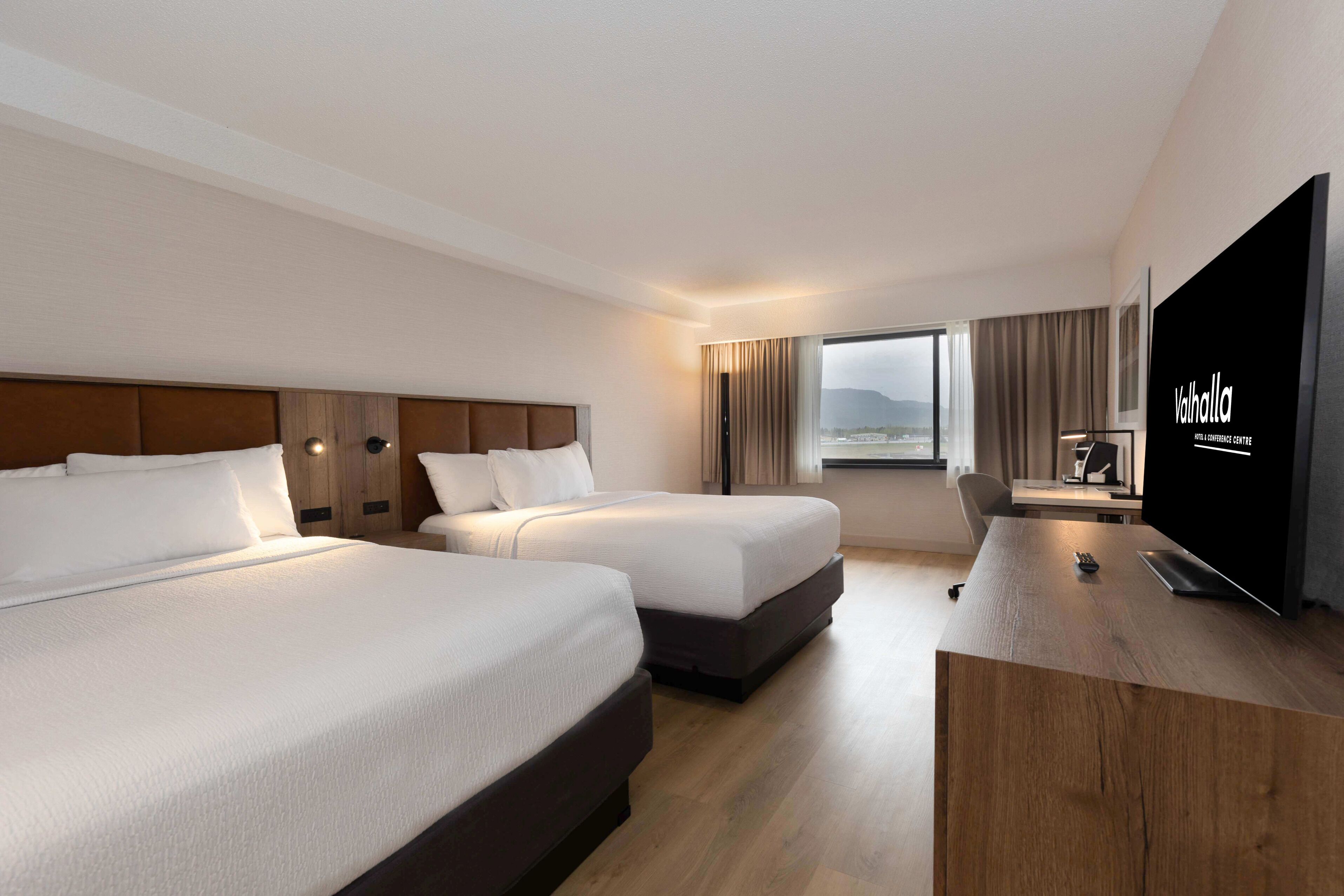 A hotel room with two beds, a desk, a TV, and a view of the outdoors.