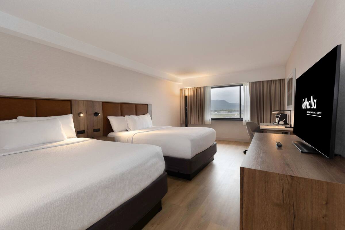 A hotel room with two beds, a desk, a TV, and a view of the outdoors.