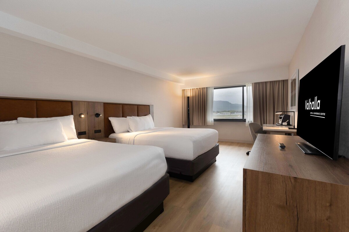 Quarto de hotel com duas camas, uma mesa, uma televisão e vista para o exterior.