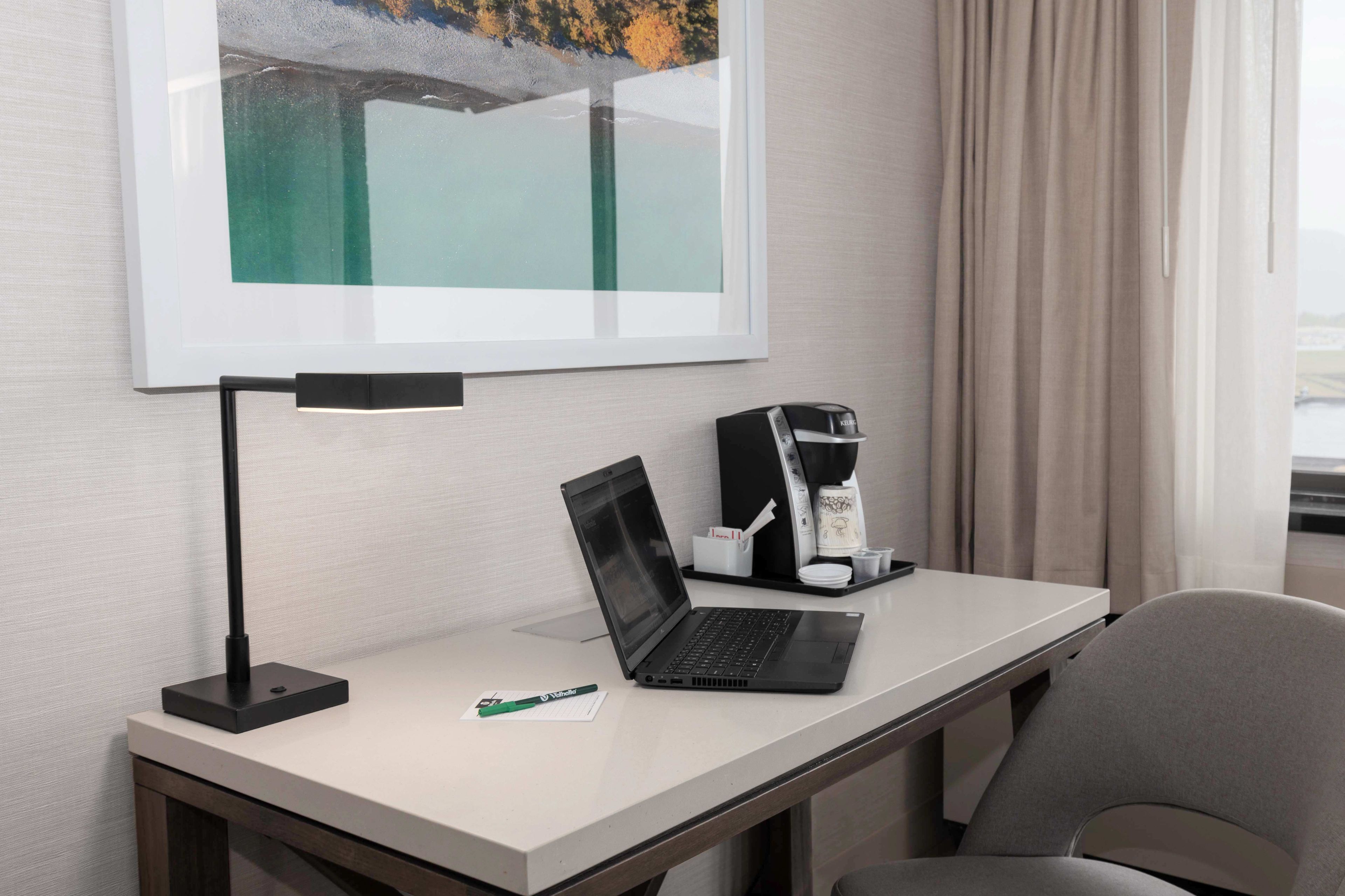Habitación de hotel con escritorio, una computadora portátil, cafetera y un cuadro en la pared.