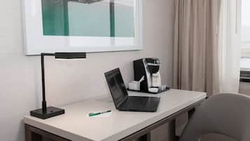 Habitación de hotel con escritorio, una computadora portátil, cafetera y un cuadro en la pared.