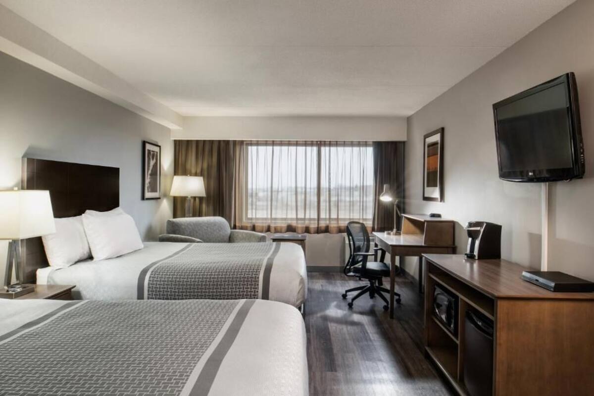 A hotel room with two beds, a desk, a chair, a television, and a window with curtains.