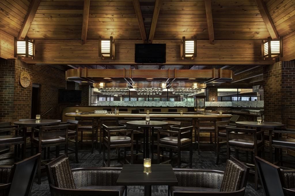 A restaurant with wooden ceiling beams, brick walls, and a bar area with glasses and bottles.