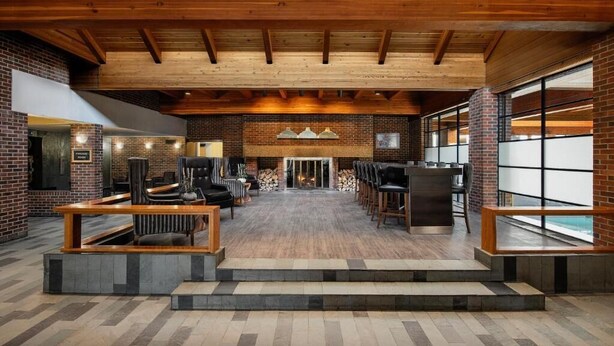 A spacious indoor area with a high ceiling, wooden beams, brick walls, and a central seating area with tables and chairs. - Valhalla Hotel and Conference Centre (Thunder Bay)