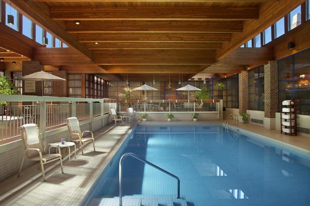 An indoor swimming pool with wooden beams, lounge chairs, and potted plants.