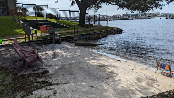 Un parque junto al río con mesas y sillas de picnic, una playa arenosa y vistas al agua.