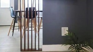 Ein modernes Wohnzimmer mit einem an der dunklen Wand befestigten Flachbildfernseher, einem Essbereich mit Stühlen und einem Tisch sowie einer Kübelpflanze.