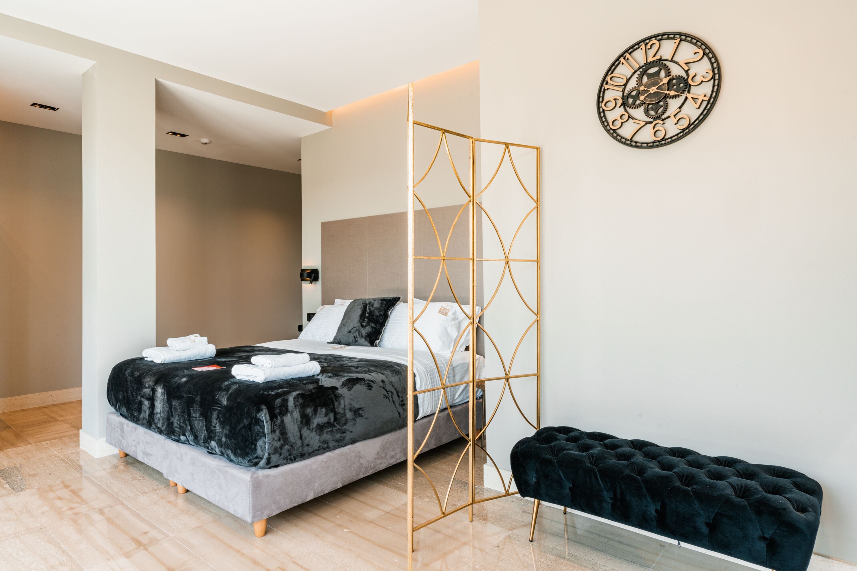 Une chambre à coucher moderne avec un lit, un banc en velours noir et une horloge murale décorative.