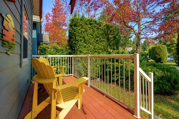 A wooden deck with a white railing, two yellow Adirondack chairs, and a house with a blue exterior.