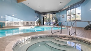 Une piscine intérieure dotée d’une terrasse carrelée, une pièce baignée de lumière avec des murs bleus et une vue sur l’extérieur grâce à de grandes fenêtres.