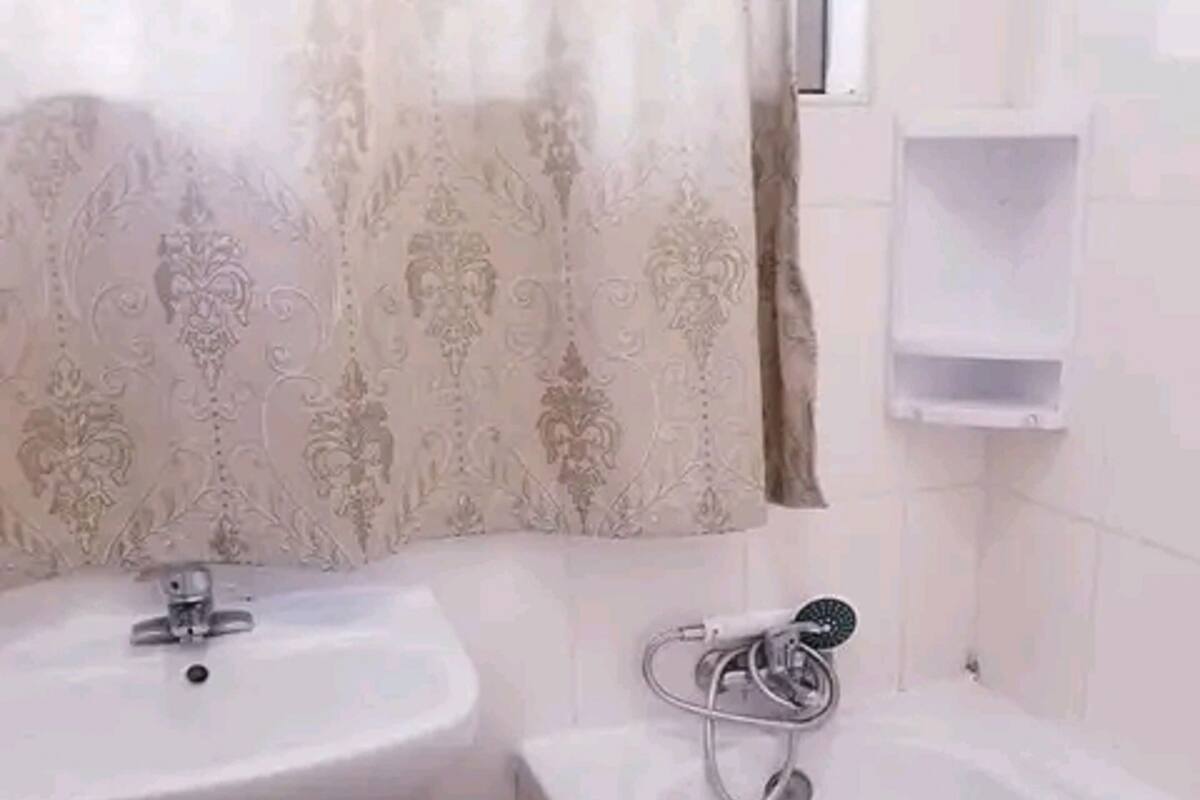 A bathroom with a white sink, a bathtub, and a toilet. There is a towel rack above the bathtub and a small shelf on the wall.