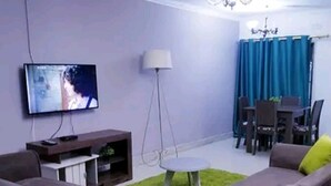 A living room with a flat-screen TV, a dining table with chairs, a chandelier, and a sofa with a green accent.