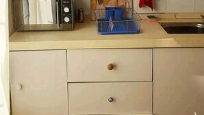 A kitchen with a microwave, a toaster, and a sink. There are cabinets with knobs and a red towel hanging on the wall.