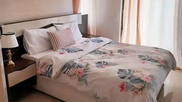 A neatly made bed with floral bedding, a bedside table with a lamp, and a window with curtains.