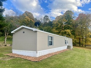 Ein Bungalow mit Satellitenschüssel, einer kleinen Veranda und einem Garten mit Mulch und Rasen.