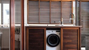 A compact laundry area with a washing machine, wooden blinds, and a sink. - The Otto at Moffat Beach (Moffat Beach)