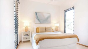 Ein Schlafzimmer mit einem Bett, Nachttischlampen, einem Nachttisch, einem Fenster und einem Wandbild.