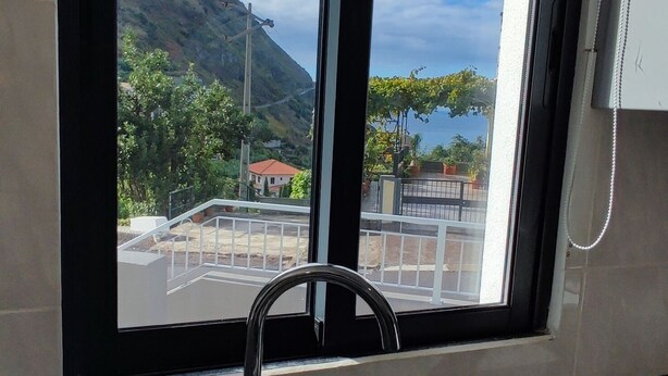 A kitchen with a stainless steel sink, a window with a view of a mountainous landscape, and a metal drying rack.