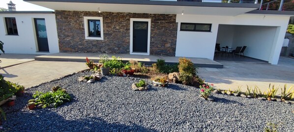 Une maison moderne avec une façade en pierre, une allée en gravier et différentes plantes en pot.