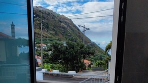 An open door leading to a balcony with a view of a hillside, a staircase, and a small building in the distance.