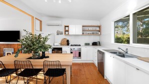 A modern kitchen with white cabinets, a wooden dining table, and black chairs. - Anglesea Beach House 2 (Anglesea)