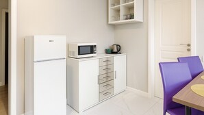 A compact kitchen with a refrigerator, microwave, and a cabinet with glass jars.