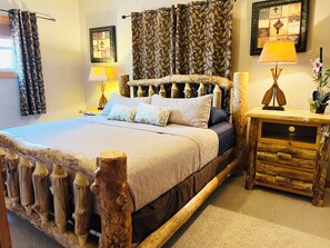 Una cama con cabecera de madera, una mesita de noche con lámpara y una pared con un cuadro enmarcado.