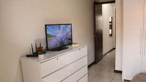 A white dresser with a flat-screen TV on top, a small plant, and a remote control. - CASA GORETE PRAIA DAS DUNAS RESIDENCE CLUB (Cabo Frio)