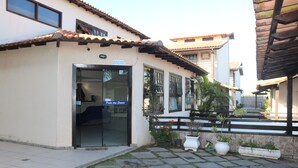 A building with a tiled roof, a glass door entrance, and potted plants. - CASA GORETE PRAIA DAS DUNAS RESIDENCE CLUB (Cabo Frio)