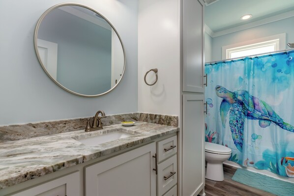 A bathroom with a marble sink, a round mirror, a toilet, and a shower curtain with a fish design. - Gulf View! 4 bathrooms! New Construction! - Southern Ties (Dauphin Island)