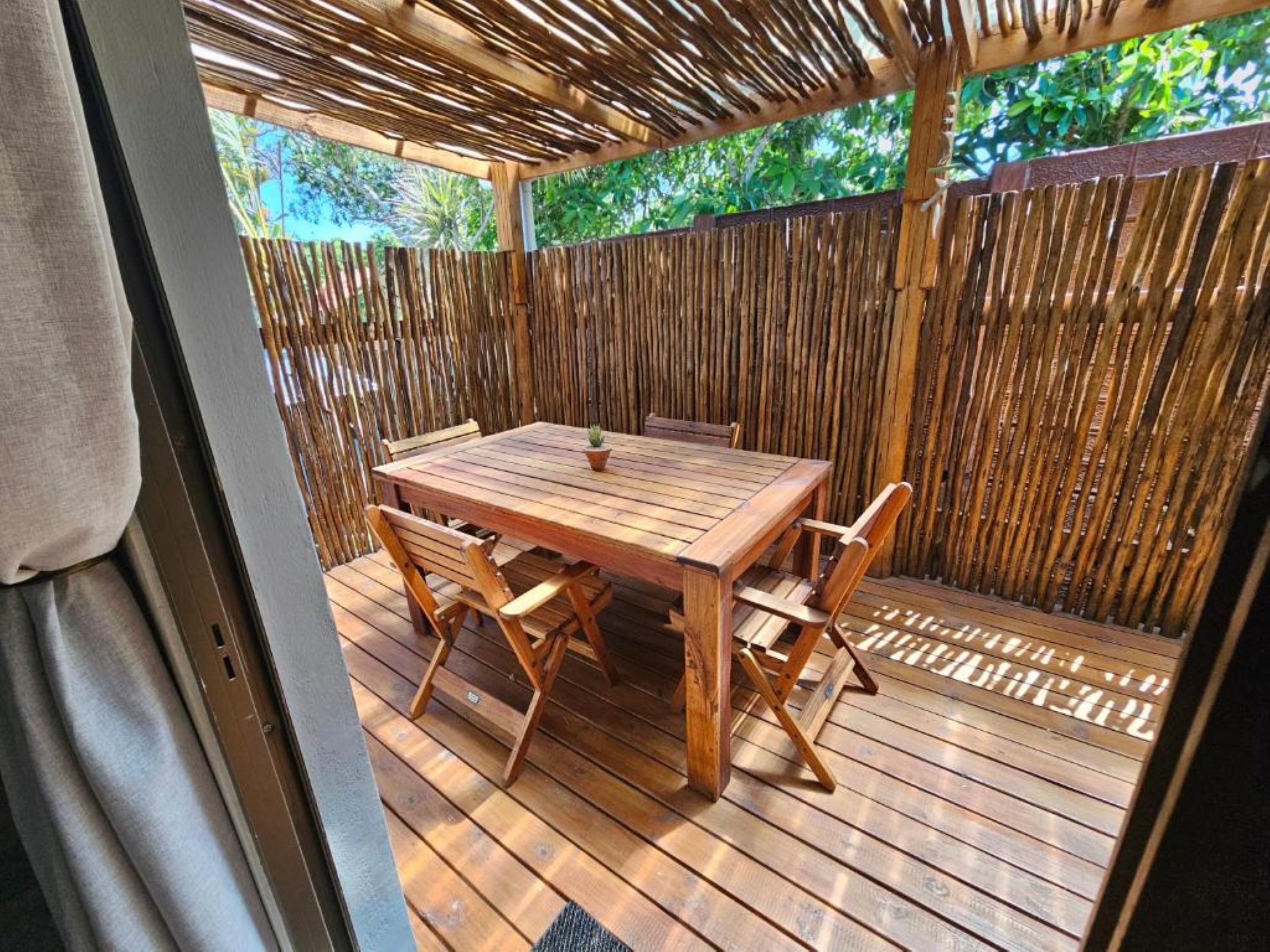 An outdoor wooden deck with a table and chairs, surrounded by a bamboo fence.