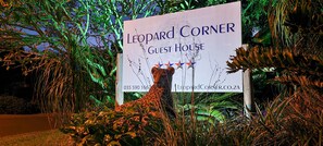 Μια πινακίδα με την ένδειξη «Leopard Corner Guest House», στην οποία αναγράφεται ένας αριθμός τηλεφώνου επικοινωνίας και η διεύθυνση της ιστοσελίδας.