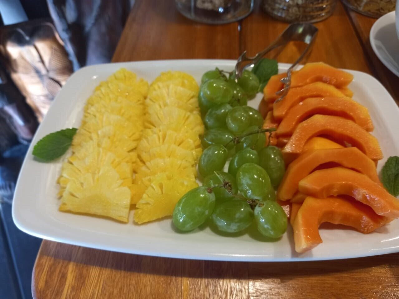 A plate with pineapple slices, green grapes, and orange fruit pieces, possibly mango, on a wooden table.