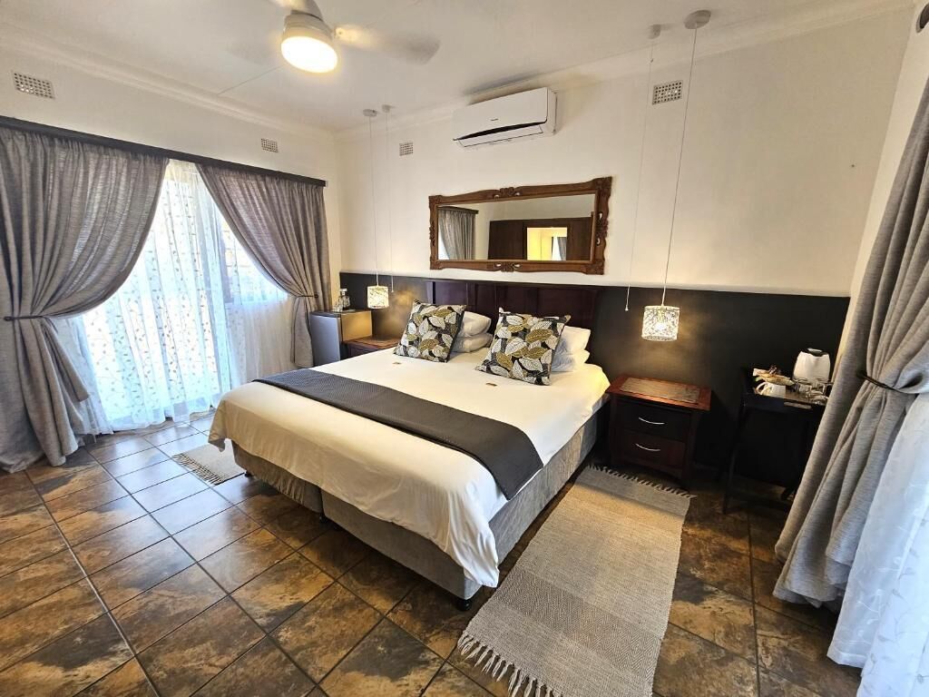 Una habitación de hotel con una cama grande, una mesita de noche, un espejo y cortinas.