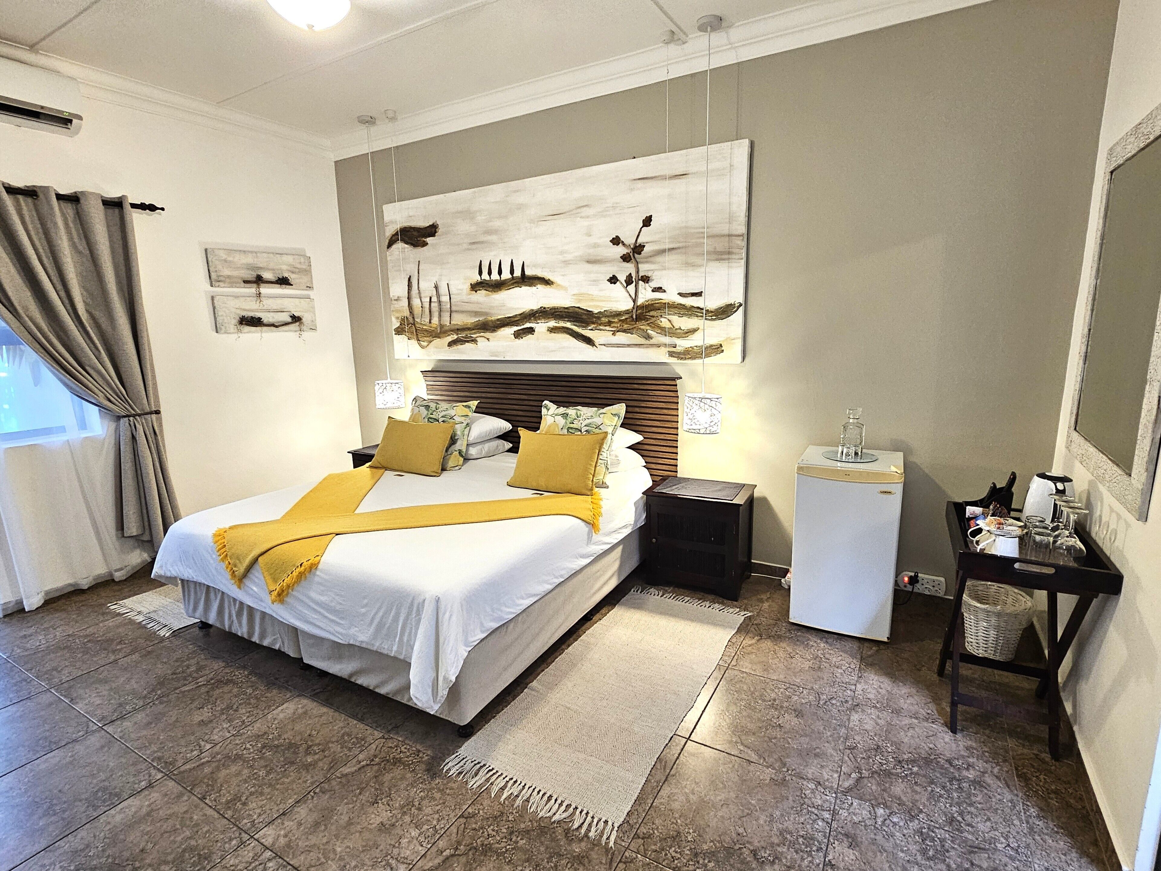 Habitación de hotel con cama, mesitas de noche, escritorio con lámpara y una obra de arte en la pared.
