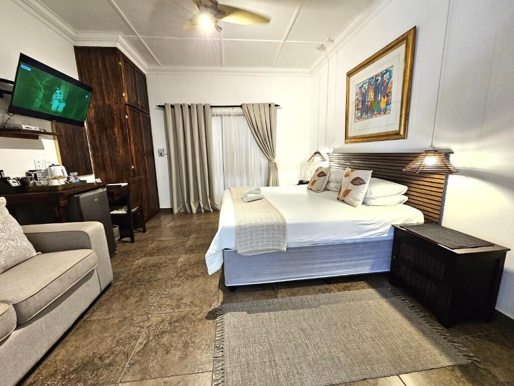Ett hotellrum med en säng, ett skrivbord, en tv, en soffa och en tavla på väggen.