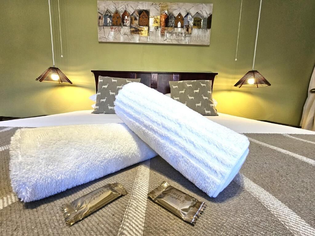 A hotel room with a bed, two bedside lamps, a painting on the wall, and a towel on the bed.