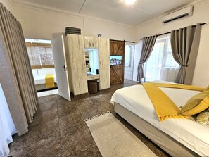 A hotel room with a bed, a wardrobe, a television, and a view of the outside. - Leopard Corner Lodge (St. Lucia)
