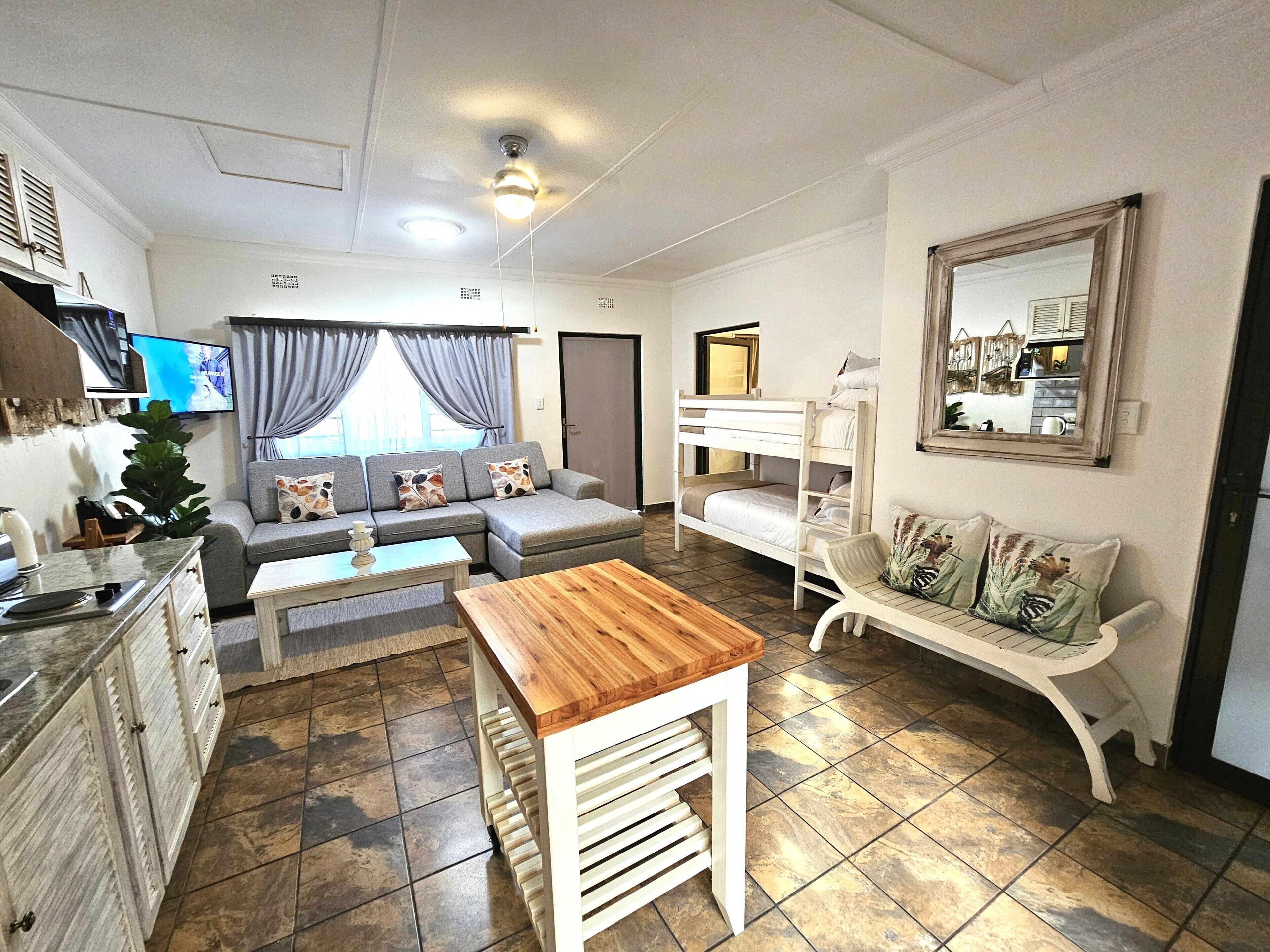 A compact living space with a sofa, a wooden table, a bunk bed, and a kitchenette.