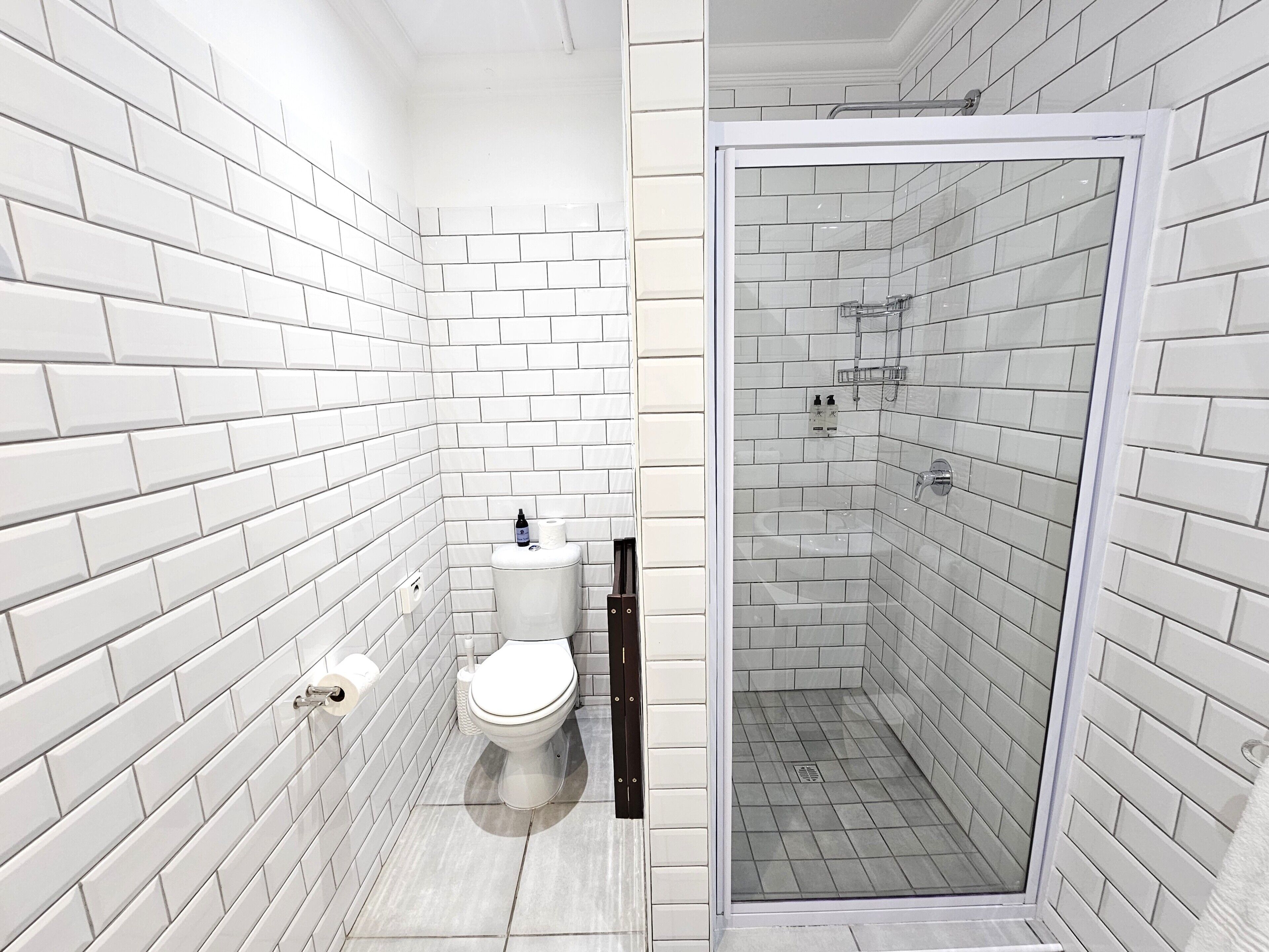 A modern bathroom with white subway tiles, a toilet, a shower with a glass door, and a sink.